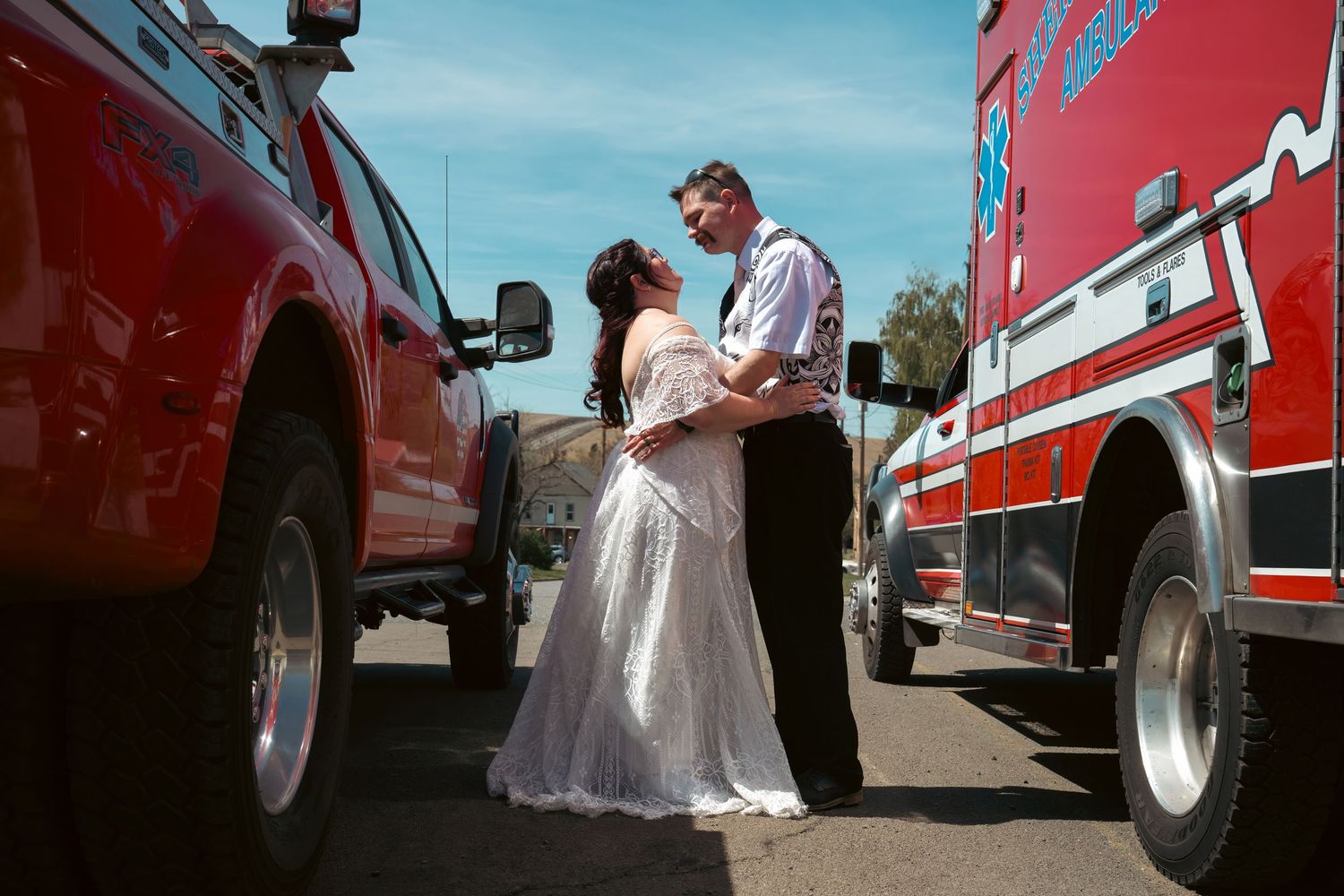 Bride and groom share romantic moment between red fire trucks at outdoor wedding ceremony.