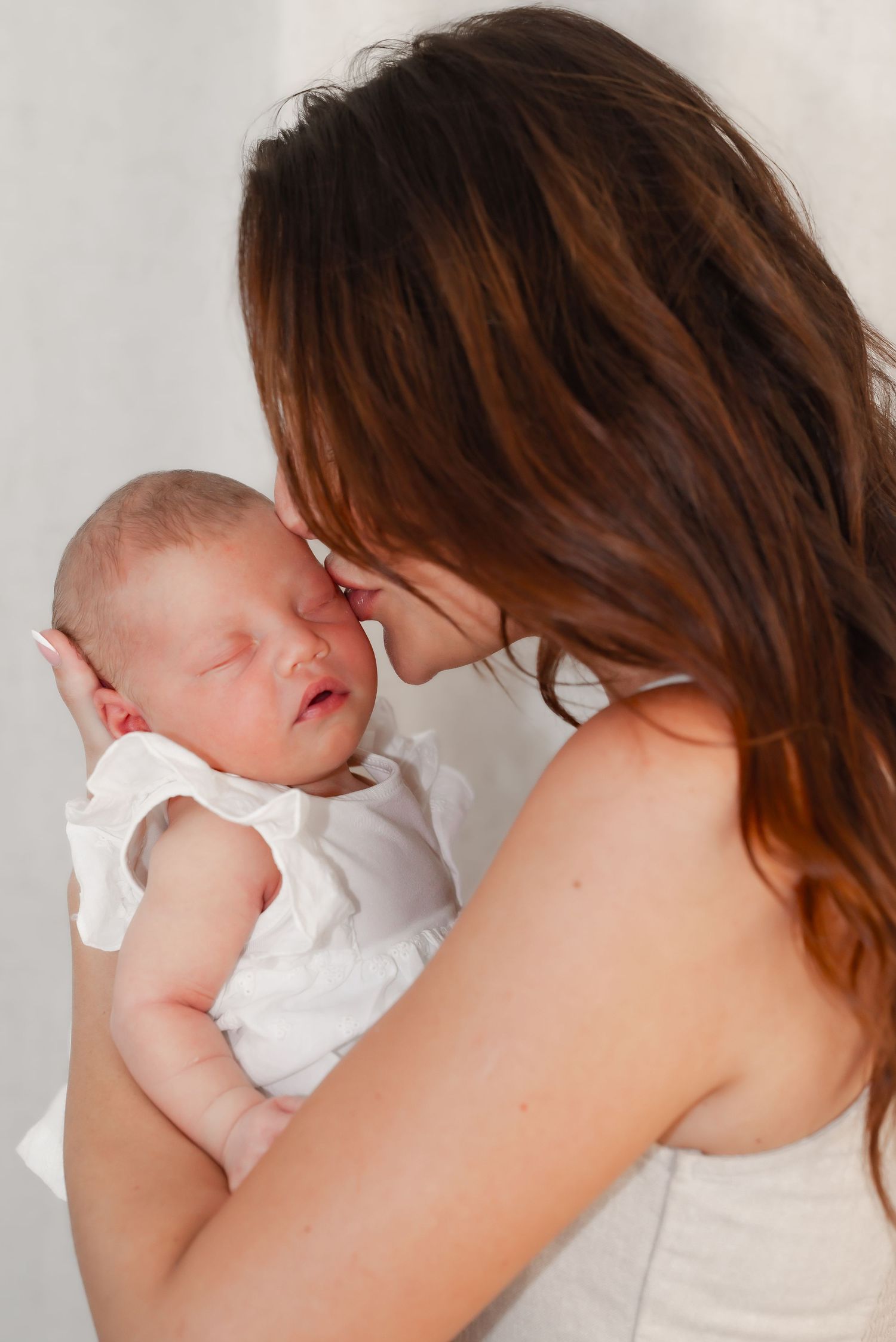 Tender moment of a mother kissing her sleeping newborn baby on the forehead.