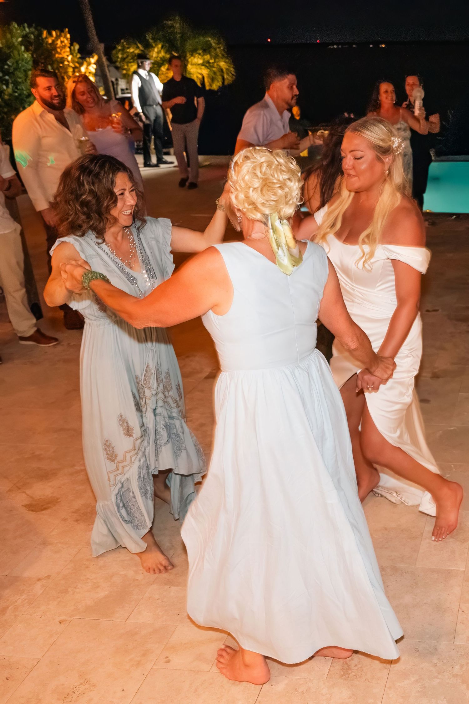 Bride dances joyfully with female guests during lively outdoor wedding reception at night.