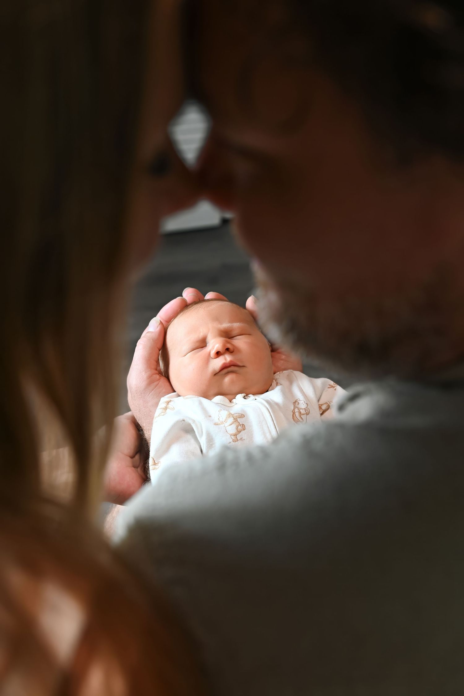 Parent tenderly cradling a sleeping newborn baby, gently placing hand on infant's head in a warm, intimate moment.