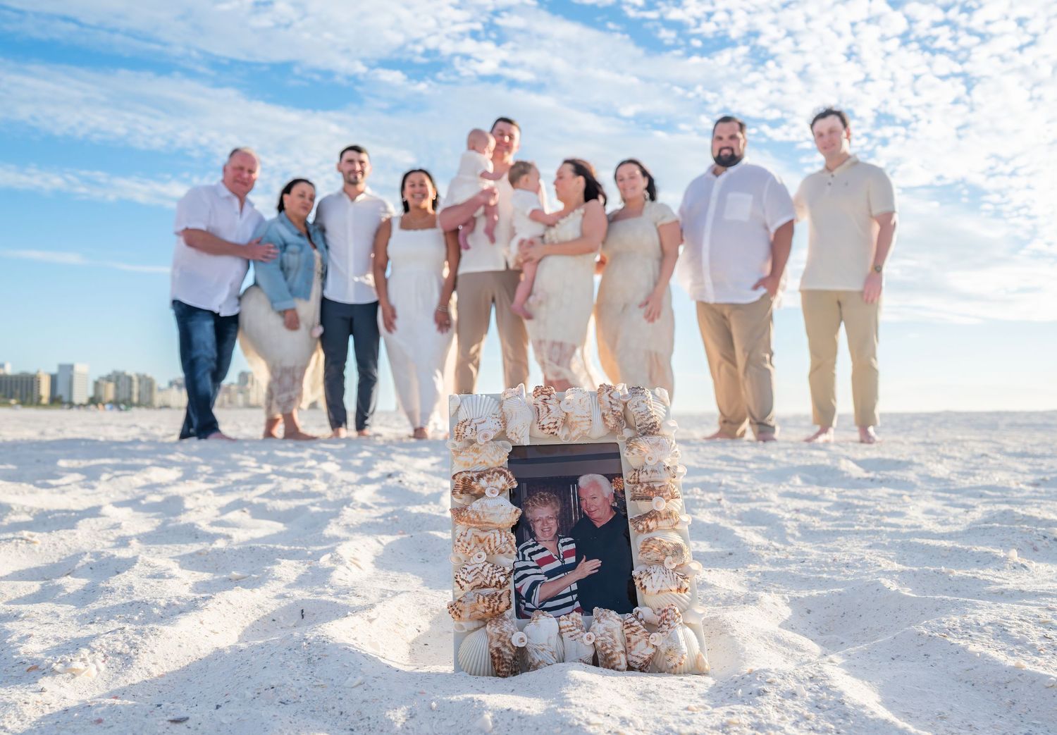 A large family group poses on white sand beach with a memorial photo display.