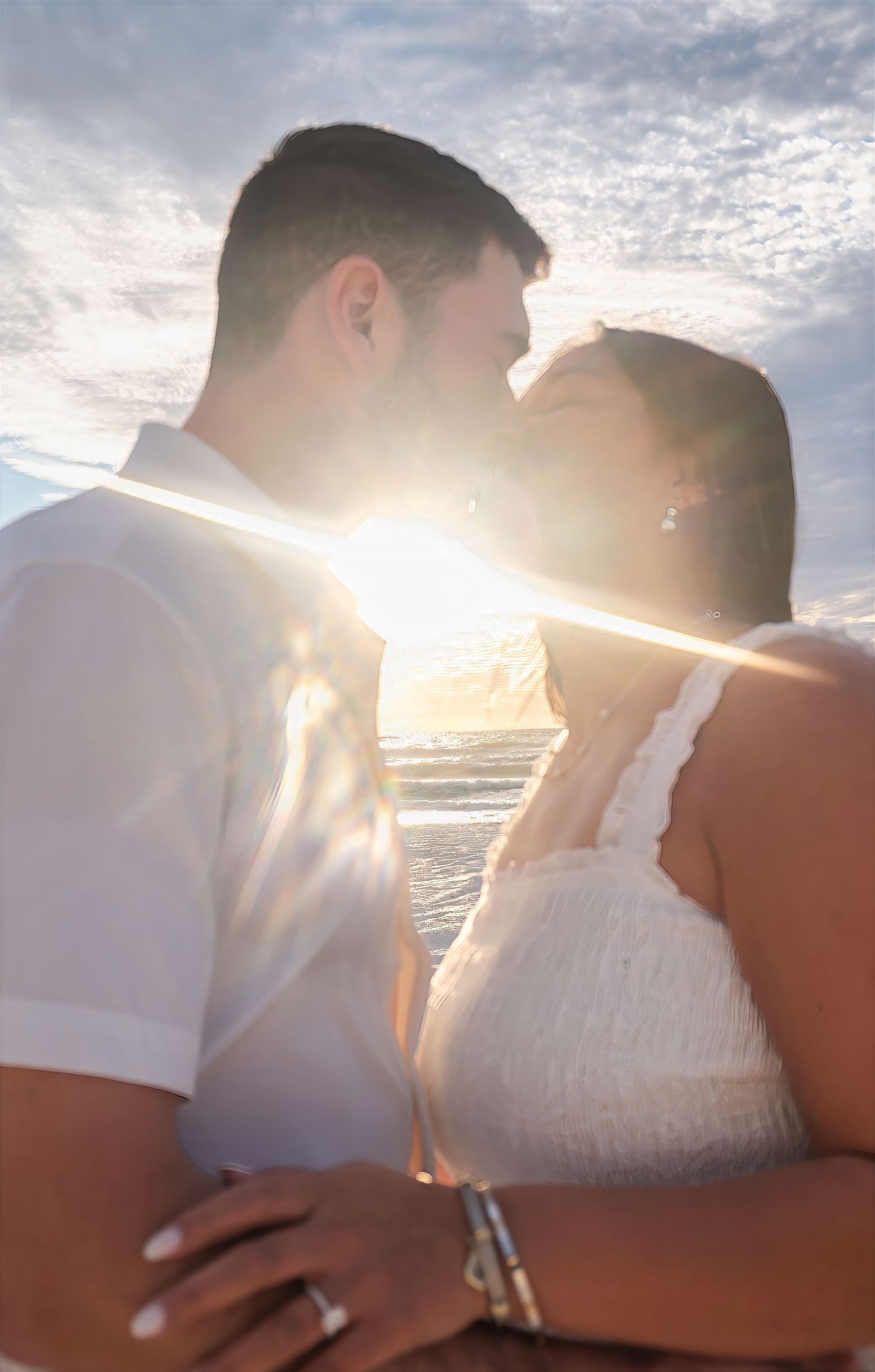 Couple kissing with sun flare at beach during golden sunset.