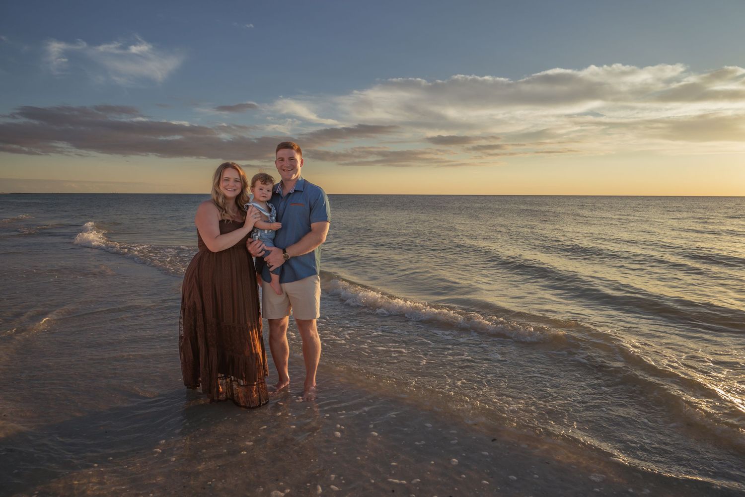 Happy family of three posing together on a sandy beach during a golden sunset.