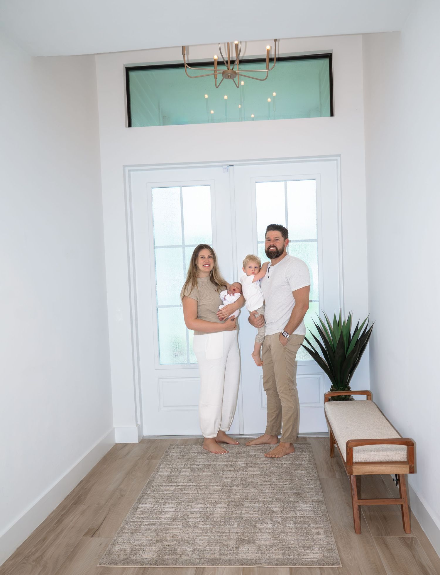 Happy family of four standing in bright modern home entryway with newborn baby.