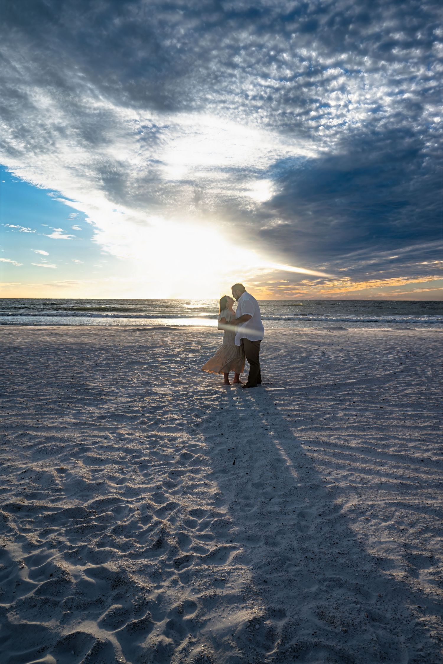 Couple embracing in silhouette on sandy beach at sunset.