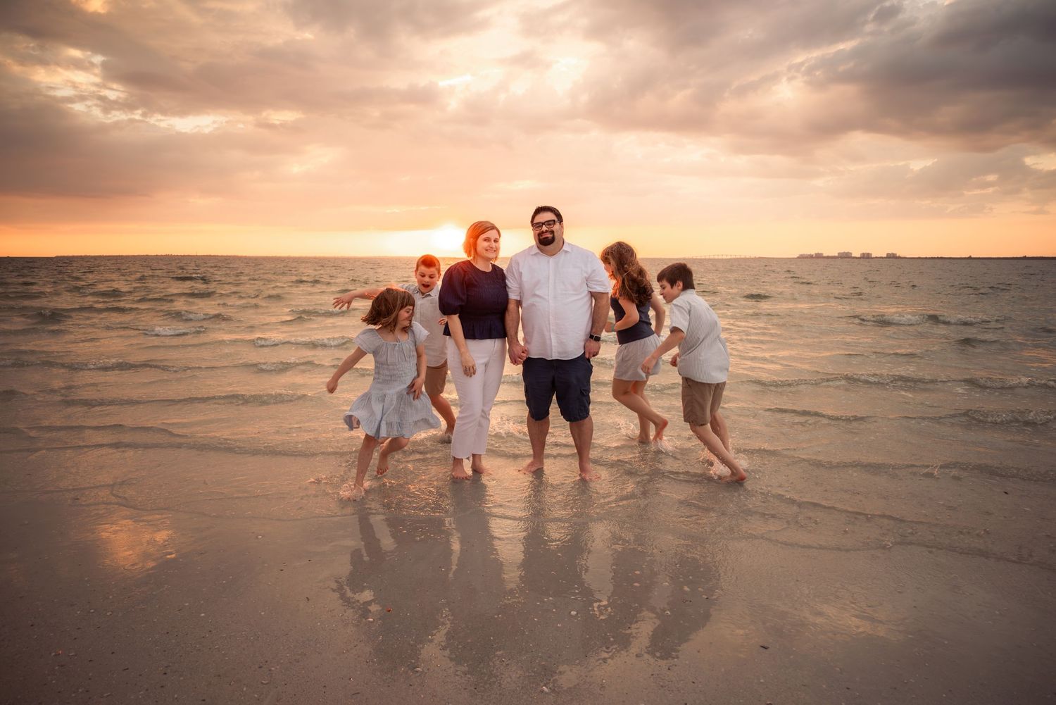 Family of five posing on a sandy beach at sunset with golden skies and ocean waves in the background.
