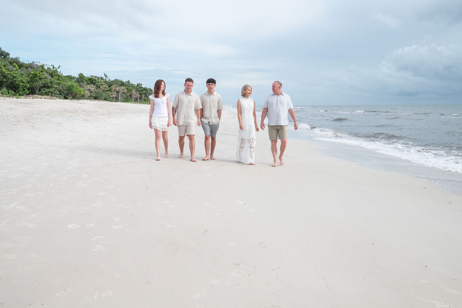 A family of five walks together on a sunny white sand beach.