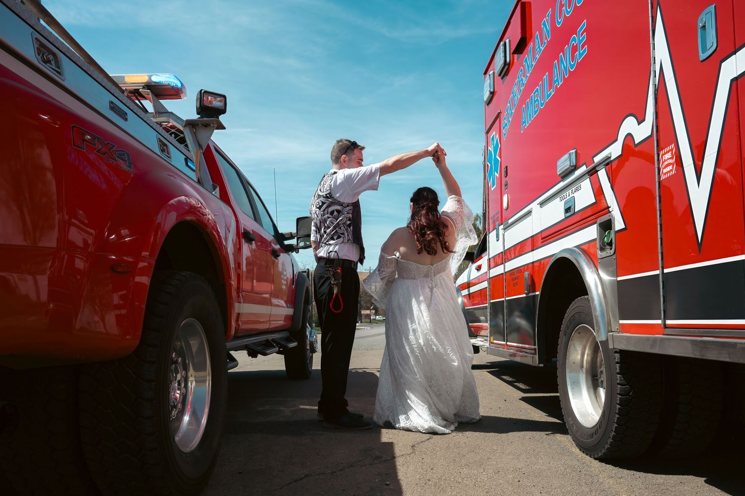 Bride and groom dancing between a red truck and ambulance on their wedding day outdoors.