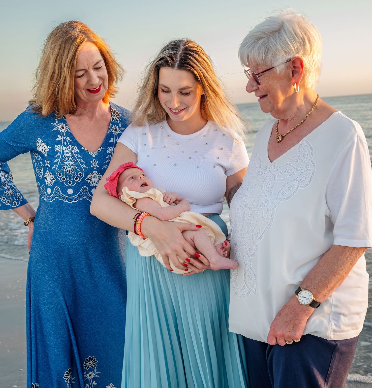 Three generations of women admire a newborn baby on a beautiful beach at sunset.