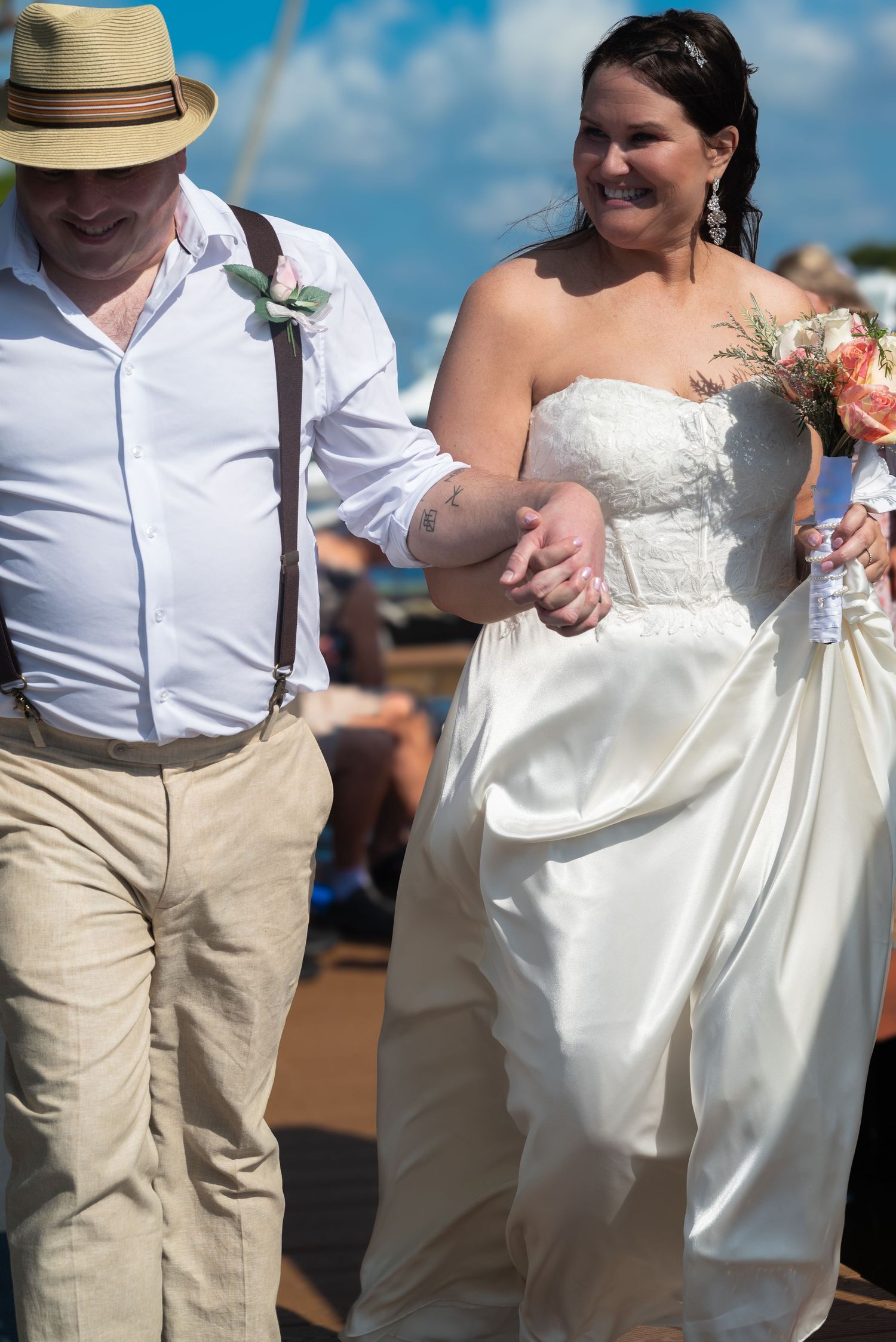 Newlywed couple walks arm in arm smiling after outdoor wedding ceremony, bride carrying bouquet.
