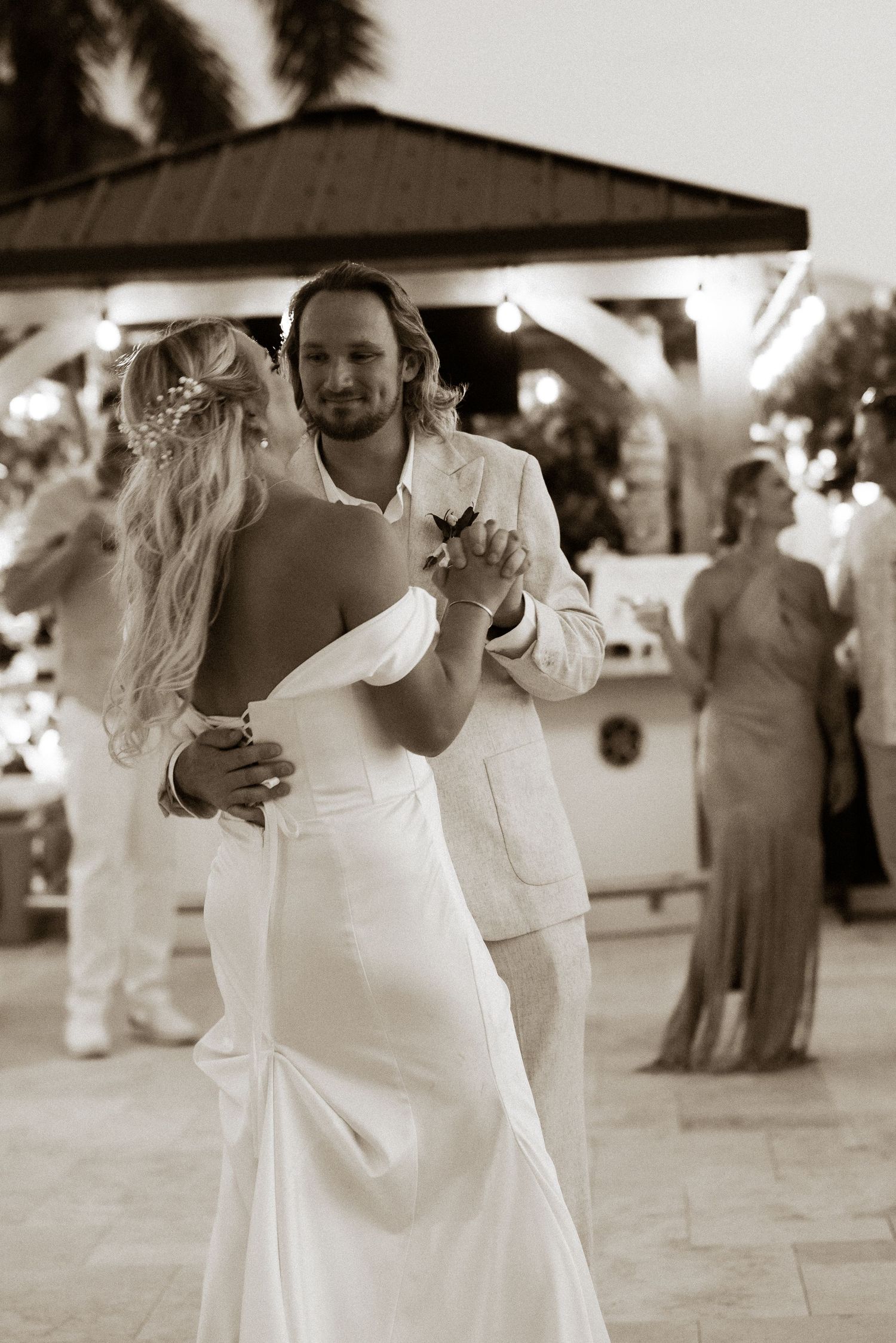 Bride and groom share their first dance at an outdoor wedding reception in a sepia-toned romantic photo.