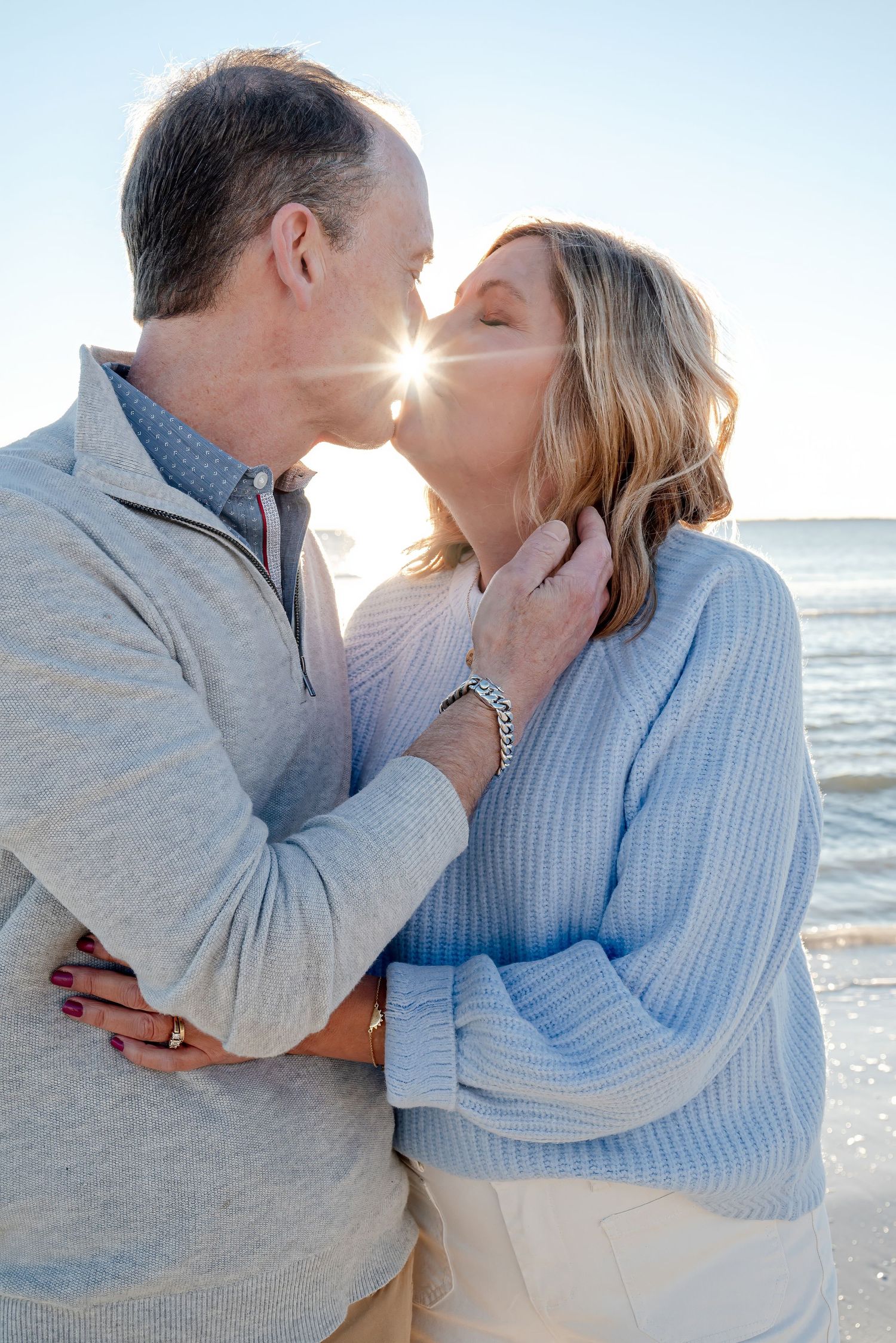 Couple sharing a romantic kiss on the beach with bright sunlight between them.
