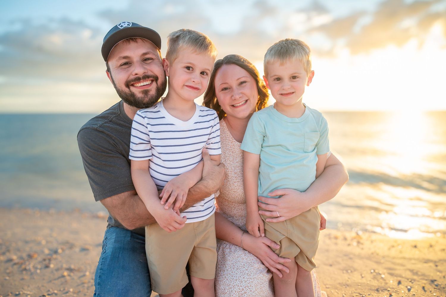 Smiling family of four posing together on sandy beach during a beautiful golden sunset.