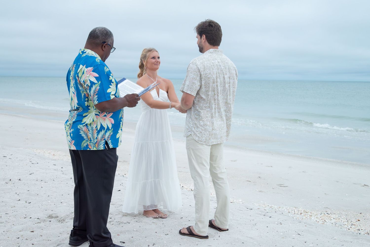Couple exchanging vows in a beach wedding ceremony with an officiant on a calm oceanfront.