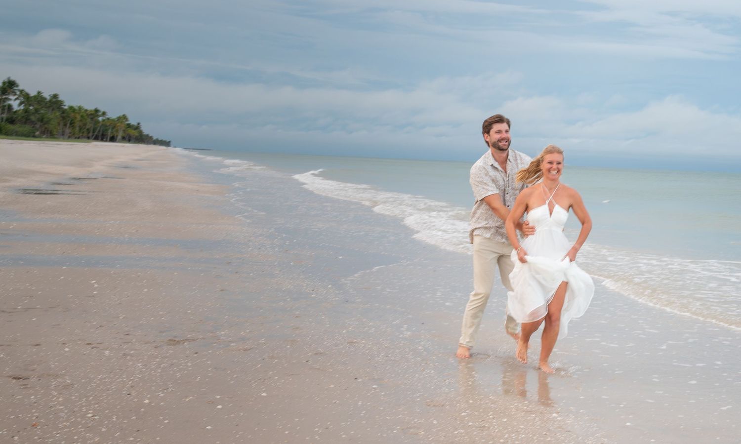 Bride and groom walking hand in hand on a tropical beach, waves gently lapping the shore on their wedding day.