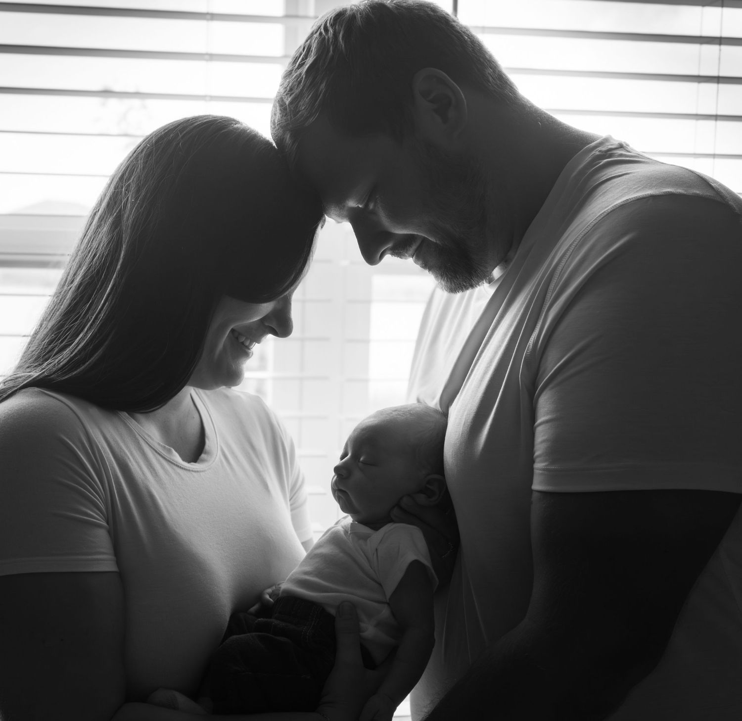 Black and white photo of new parents tenderly looking down at their newborn baby.