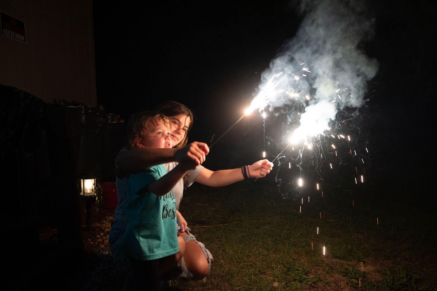 A child holds sparklers at night, creating bright light trails in the dark.
