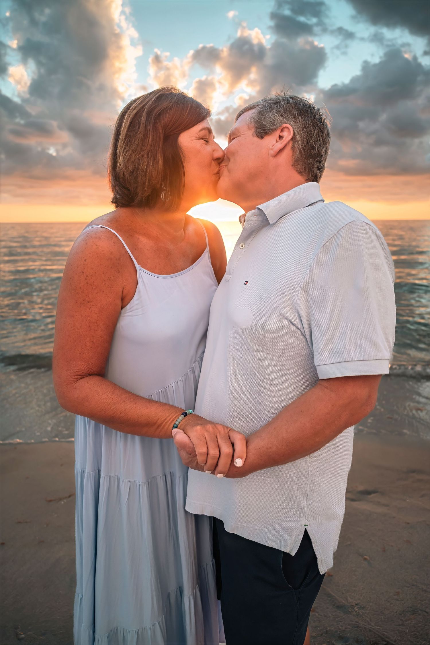 Couple sharing a tender kiss on the beach with a stunning sunset backdrop.