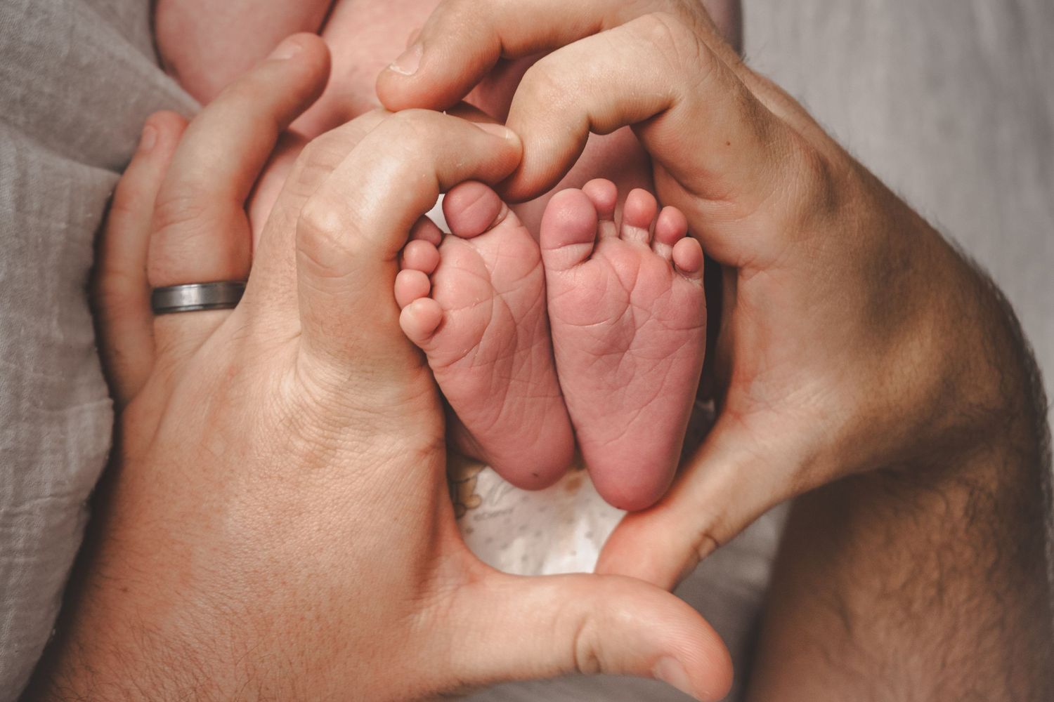 Parents forming a heart shape with their hands around their newborn baby's tiny feet.