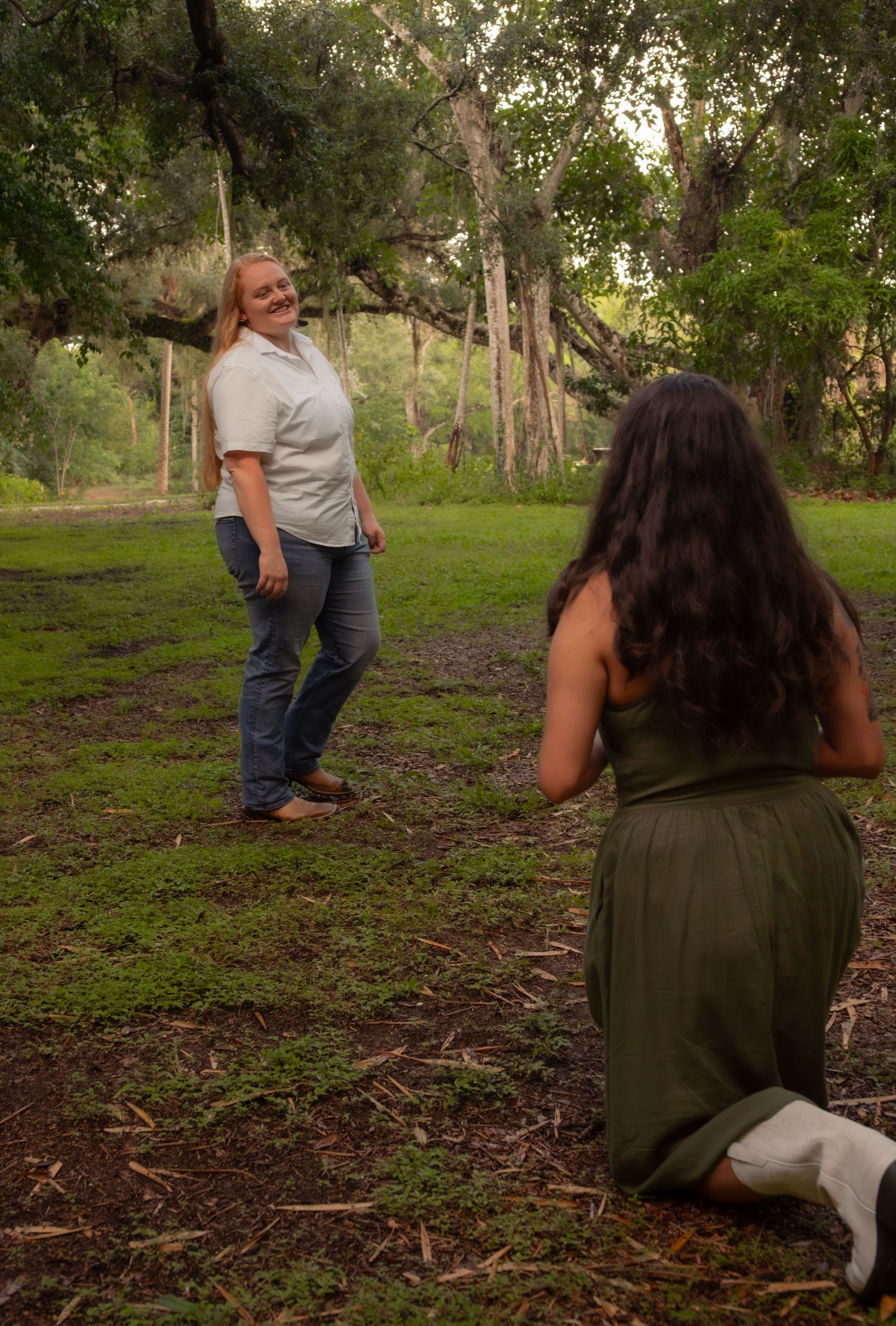 Two women in casual attire sharing a candid moment in a lush green outdoor park setting.