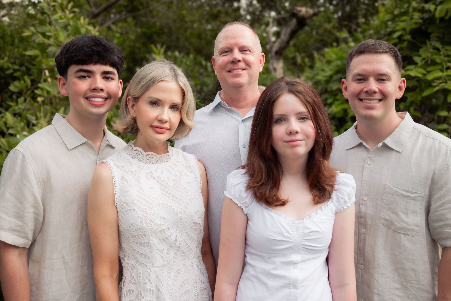 A family of five poses together outdoors in neutral tones.
