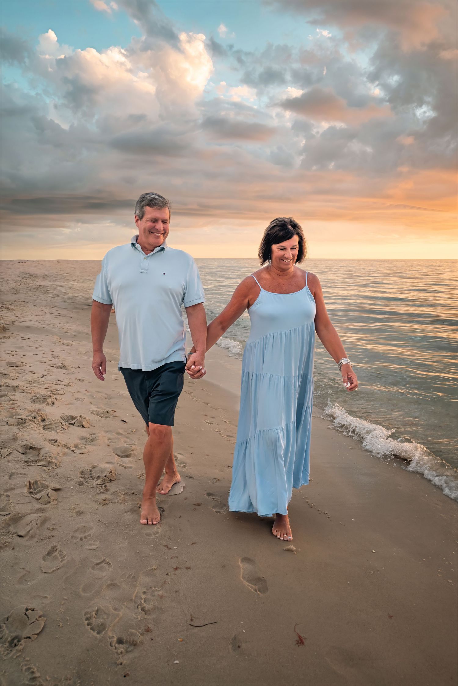 Happy couple walking hand-in-hand along a sandy beach during a colorful sunset.