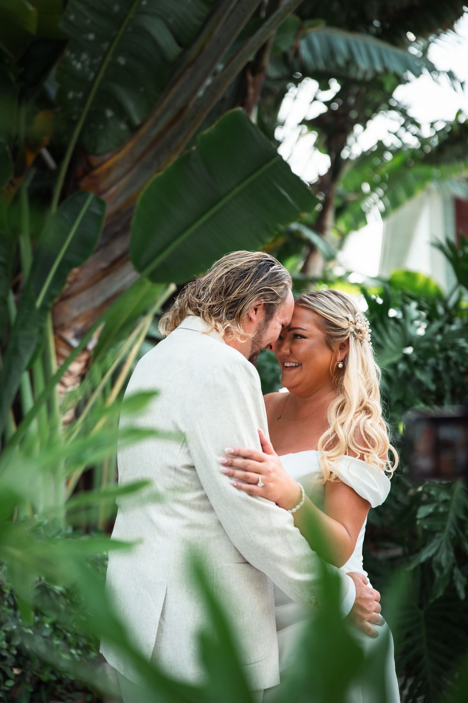 Newlyweds share an intimate forehead touch while embracing in a lush tropical garden on their wedding day.