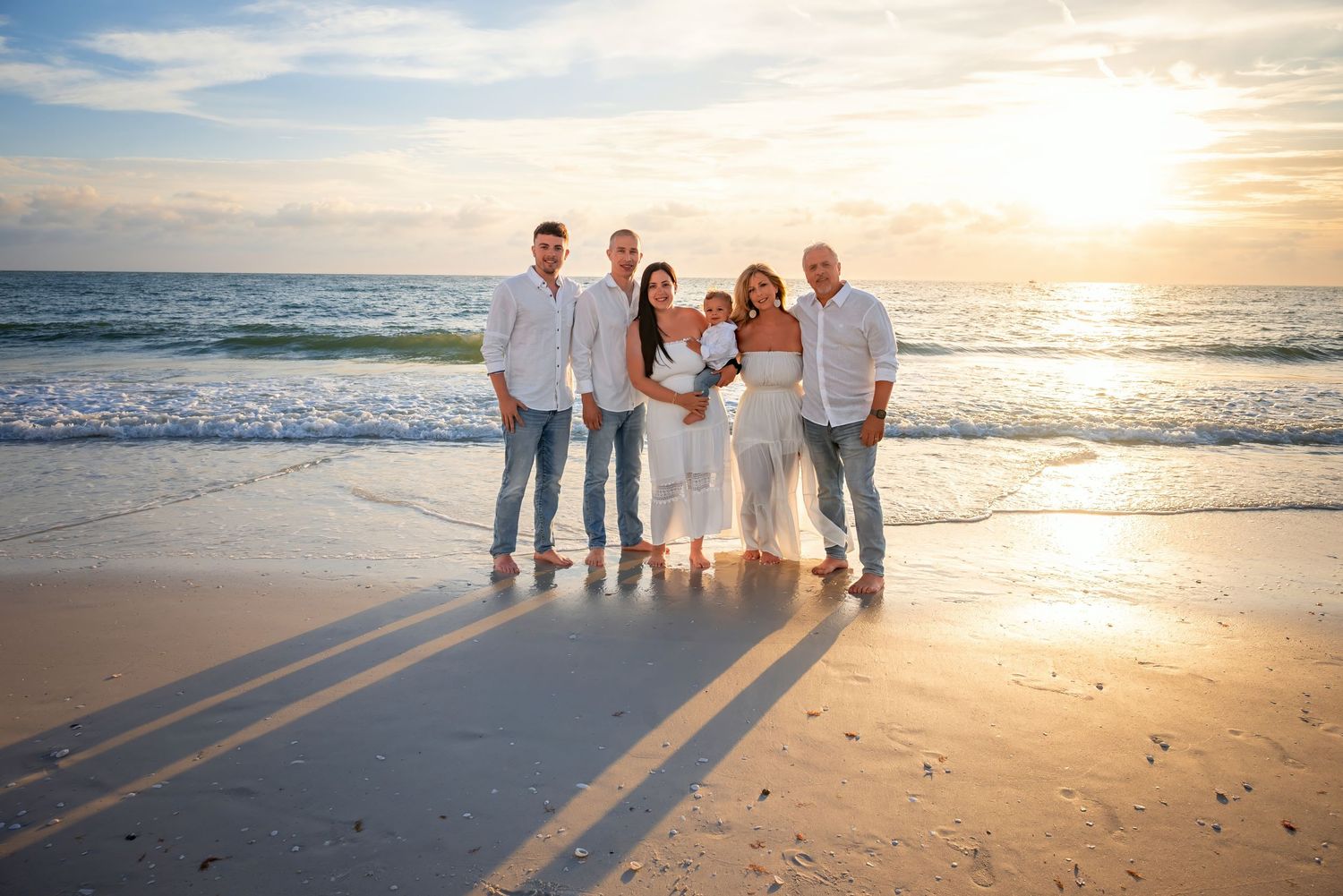 Family of six posing together on a sandy beach at golden sunset with ocean waves in the background.