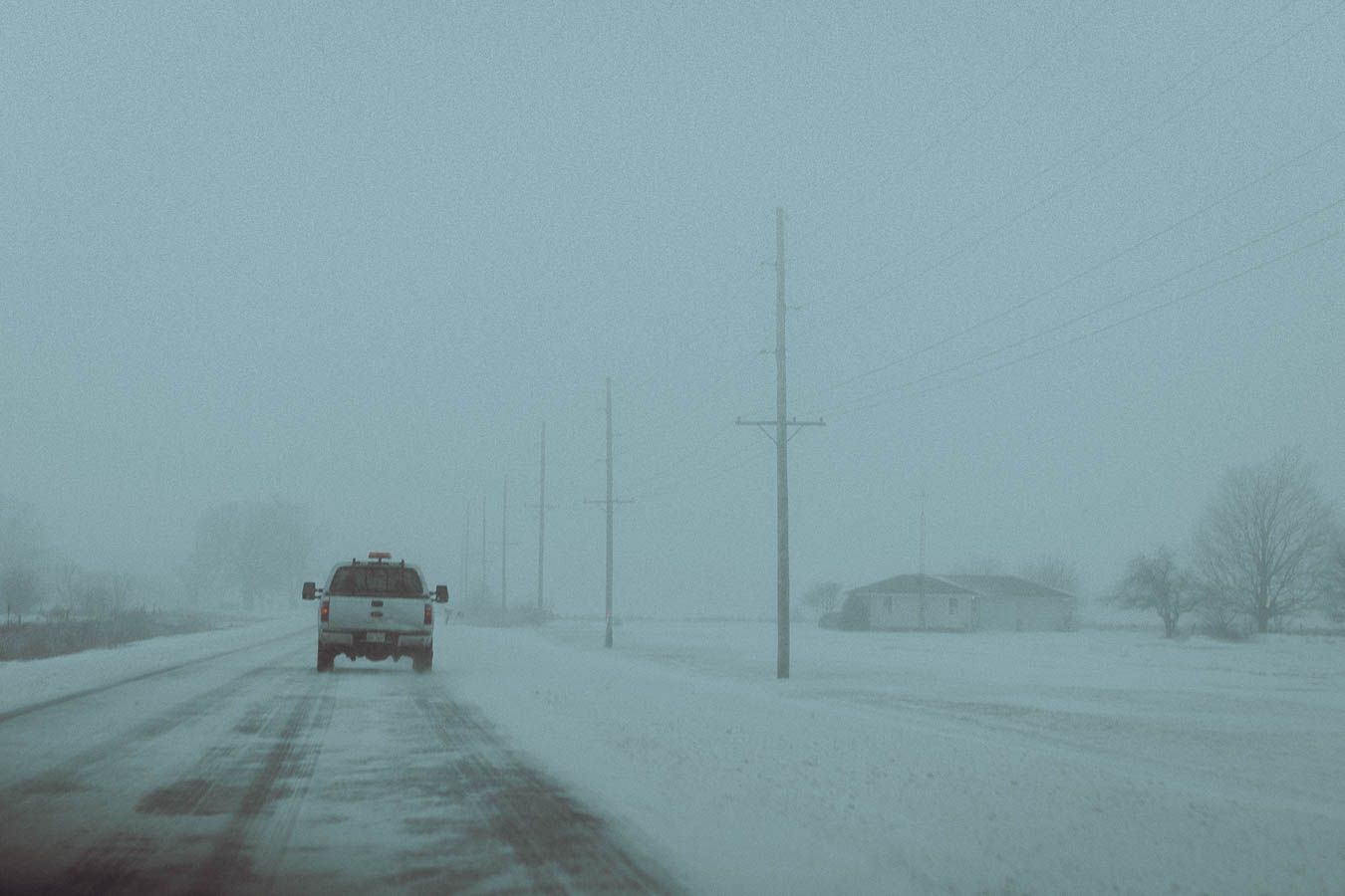 Car drives along a snowy rural road in whiteout blizzard conditions with poor visibility.