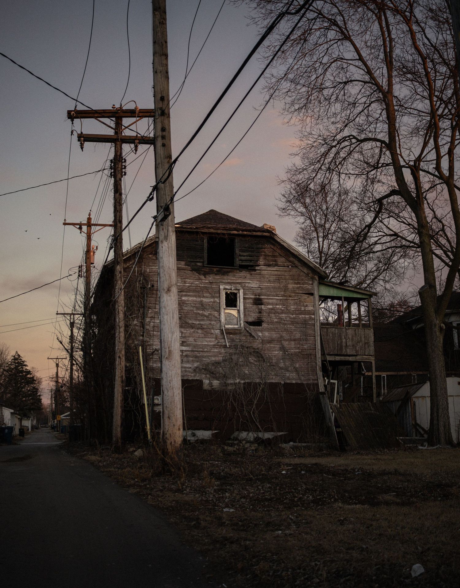 Eerily quiet urban alley at dusk with utility poles and abandoned buildings casting dark shadows.