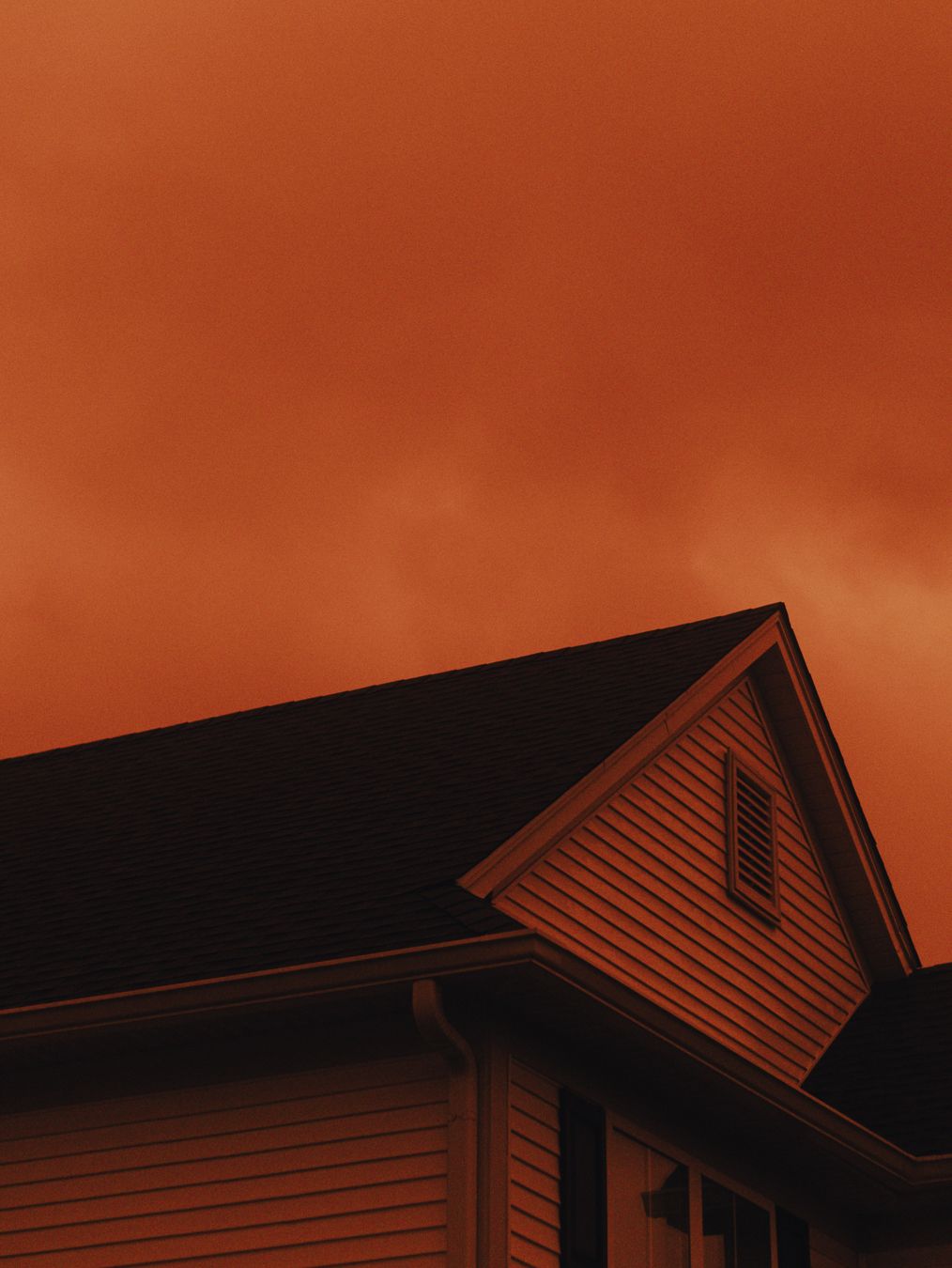House rooftop against an ominous deep orange smoky sky, suggesting wildfire or severe weather conditions.