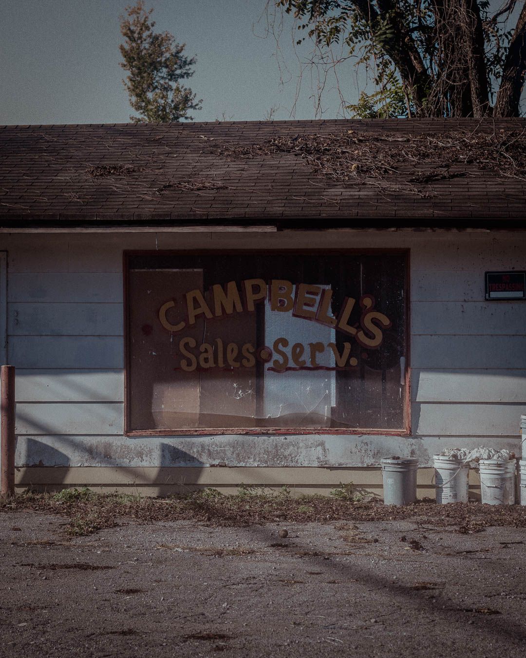 A row of abandoned storefronts with faded signs and boarded up windows in a derelict strip mall.