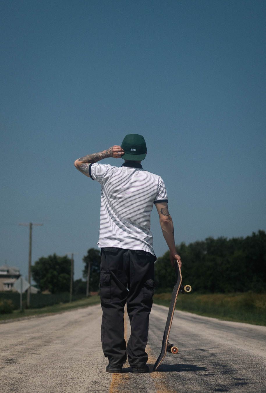A skateboarder in a white t-shirt performs tricks on a rural dirt road on a sunny day.