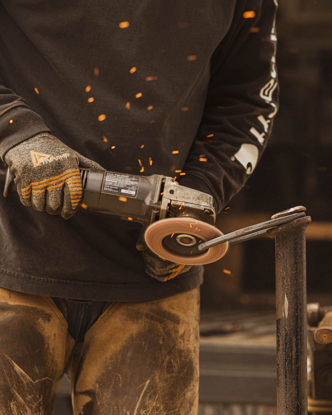 Worker using an angle grinder with protective gloves creating sparks while cutting metal in a workshop.
