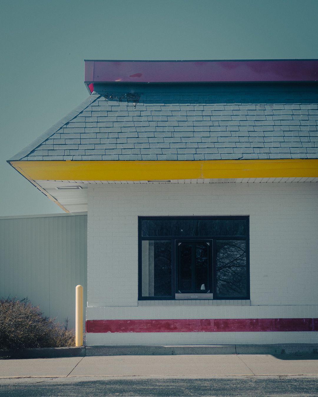 Minimalist architectural detail showing white exterior walls with pink and yellow accent stripes on a commercial building.