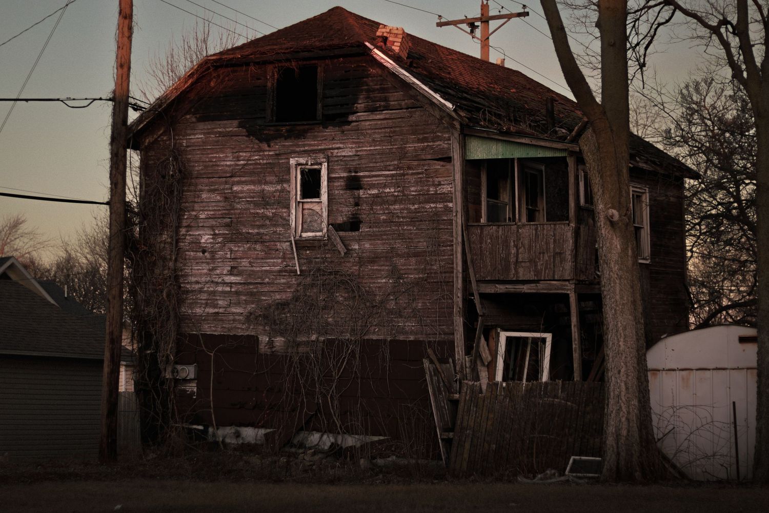 A series of weathered wooden houses and barns in various states of disrepair stand against a winter sky.