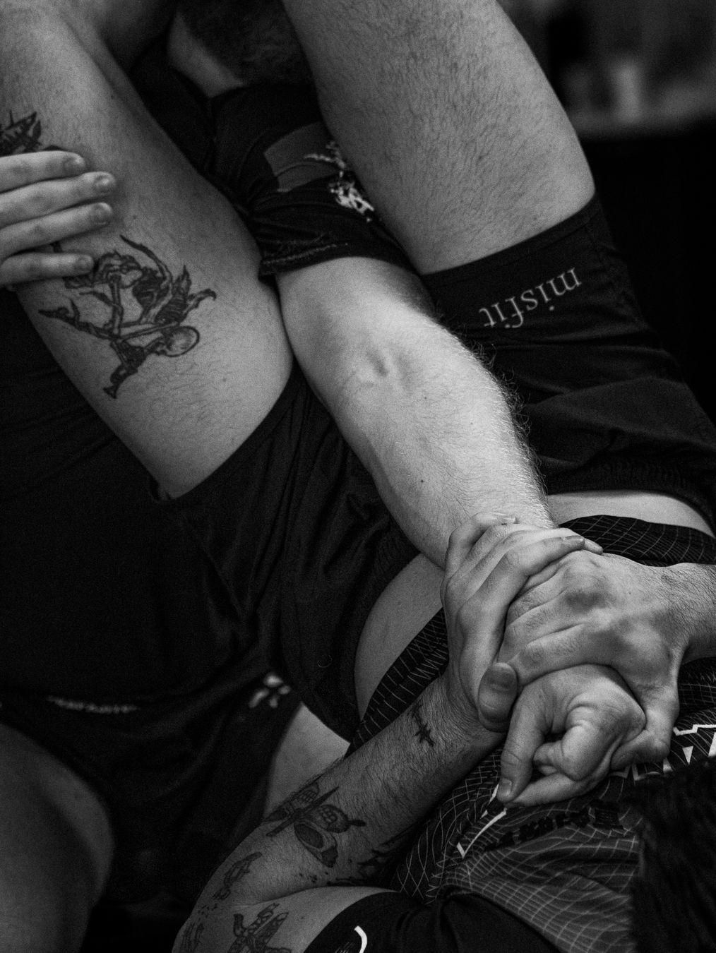 Black and white photo of tattooed arms grappling during a martial arts match, with a misfit wristband visible.
