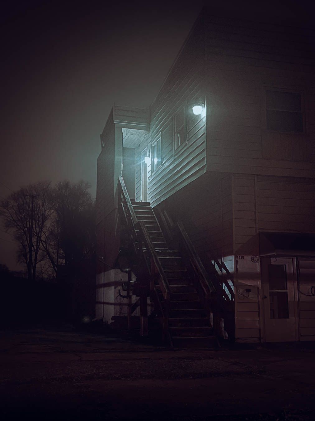 Foggy night view of an illuminated exterior staircase on a building with moody lighting and dark atmosphere.