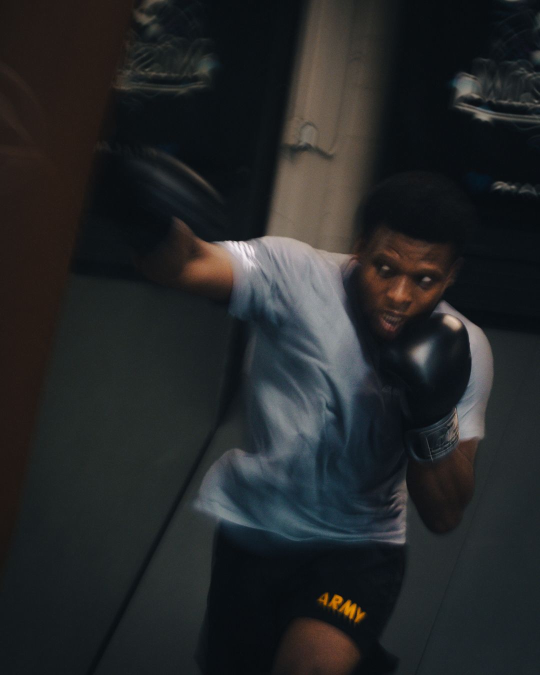 Army boxer in white tee and black gloves training on a heavy bag in a gym.
