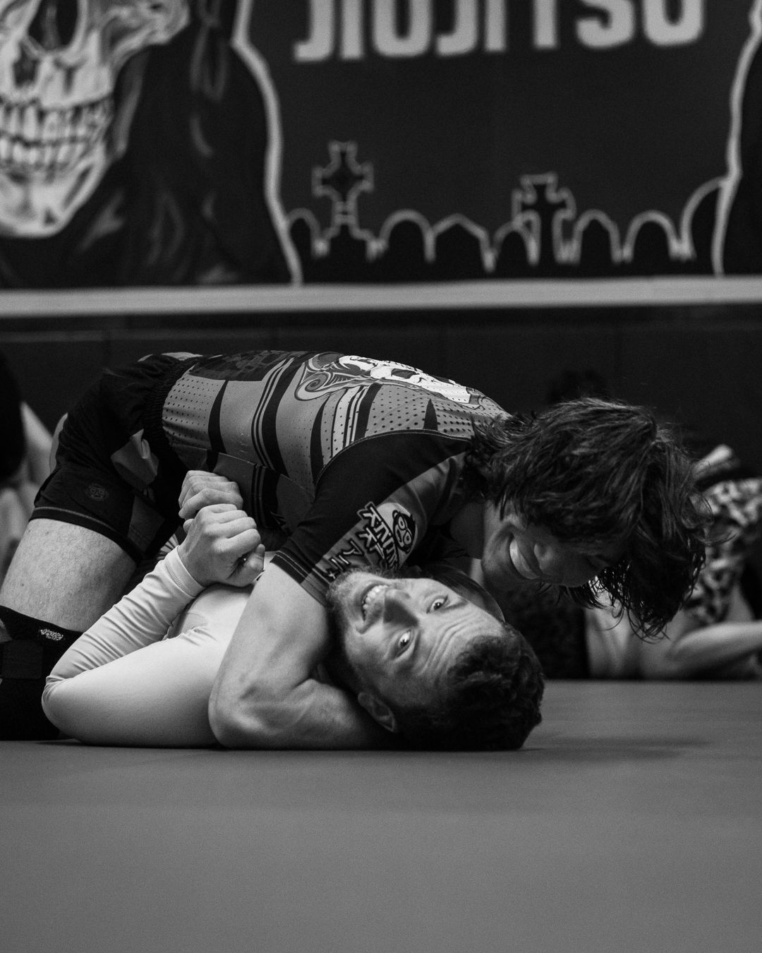 Two BJJ competitors grappling on the mat during a jiu-jitsu match in black and white photography.