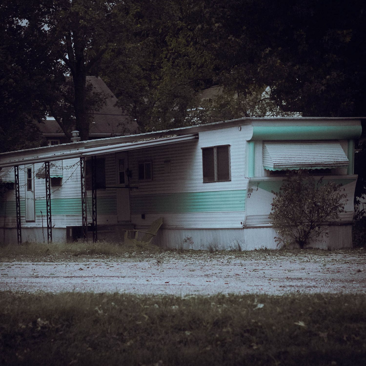 A vintage mint green mobile home trailer sits abandoned in a wooded area with snow on the ground.
