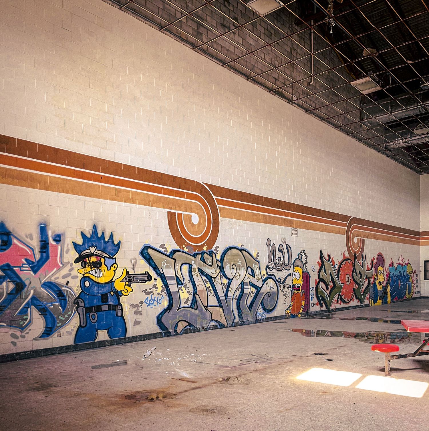 Long concrete wall covered in colorful graffiti art stretches down an empty industrial hallway with exposed ceiling.