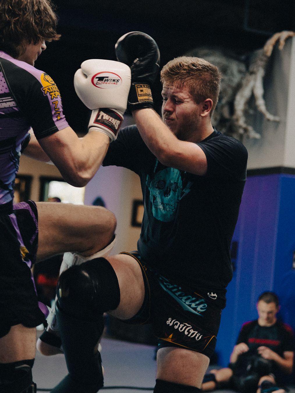 Two fighters sparring in a boxing gym, one throwing a punch while the other blocks wearing white boxing gloves.