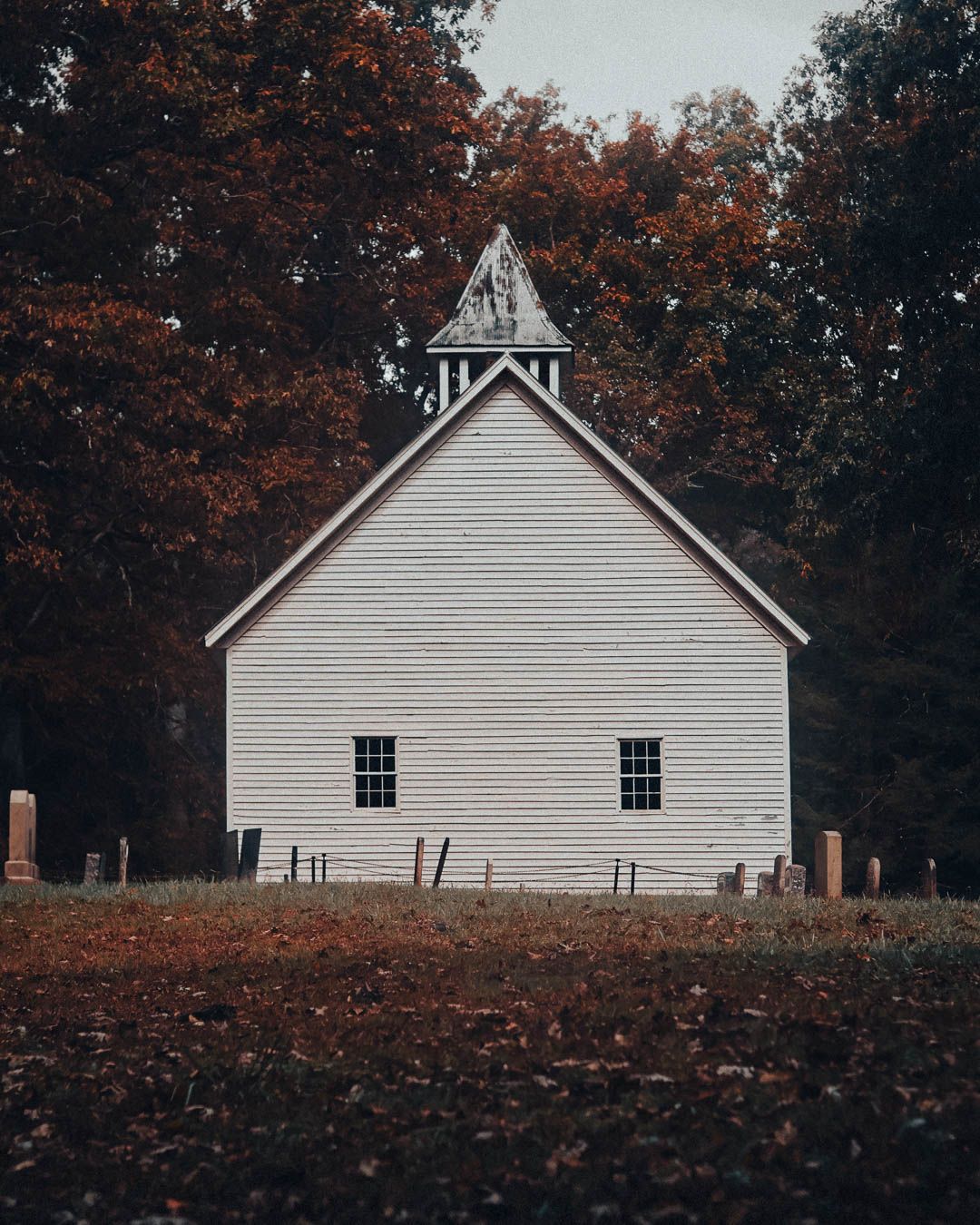 A rustic white clapboard church building photographed from different angles against autumn trees in the background.