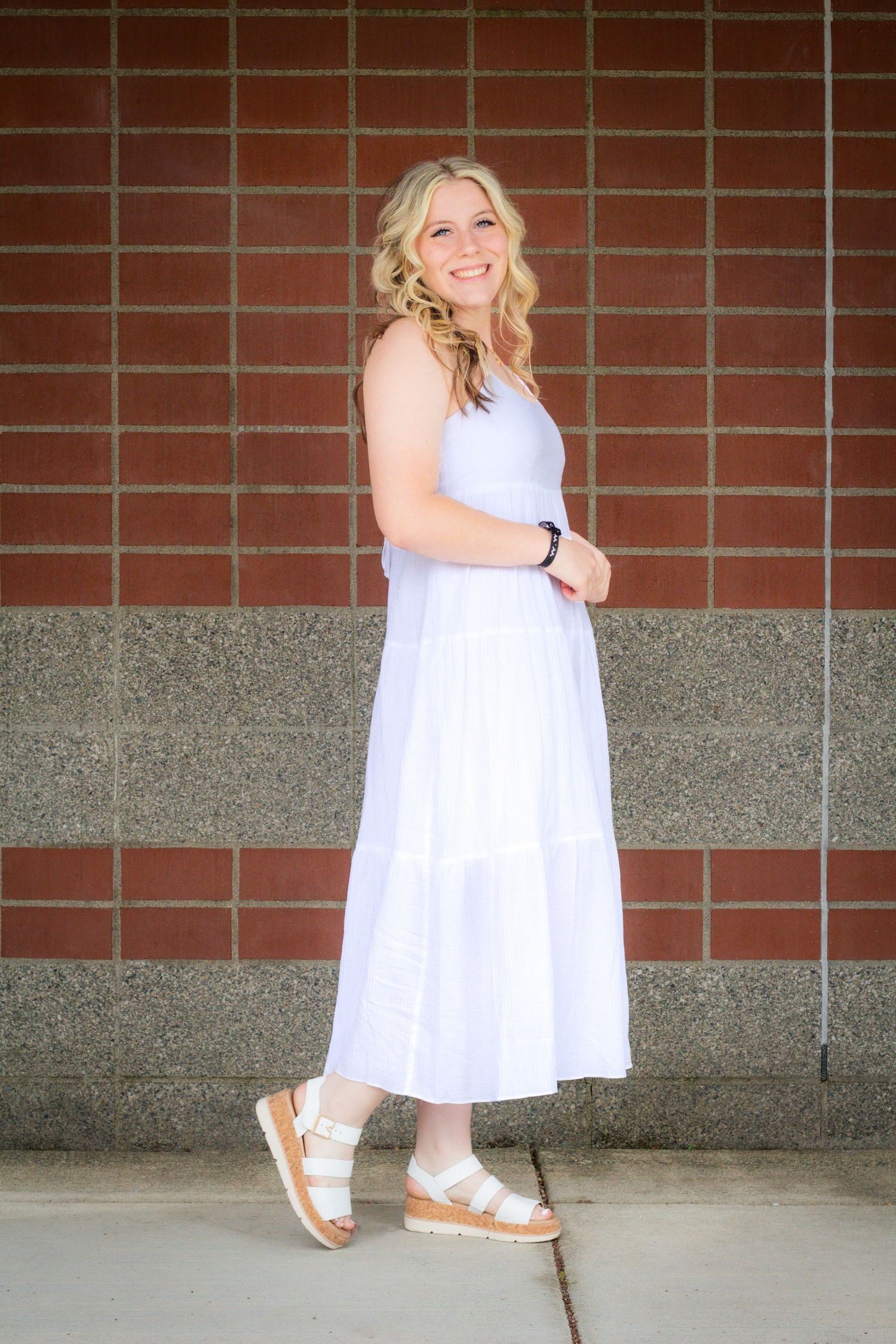 A summer portrait against a brick wall featuring a white tiered dress and platform sandals.