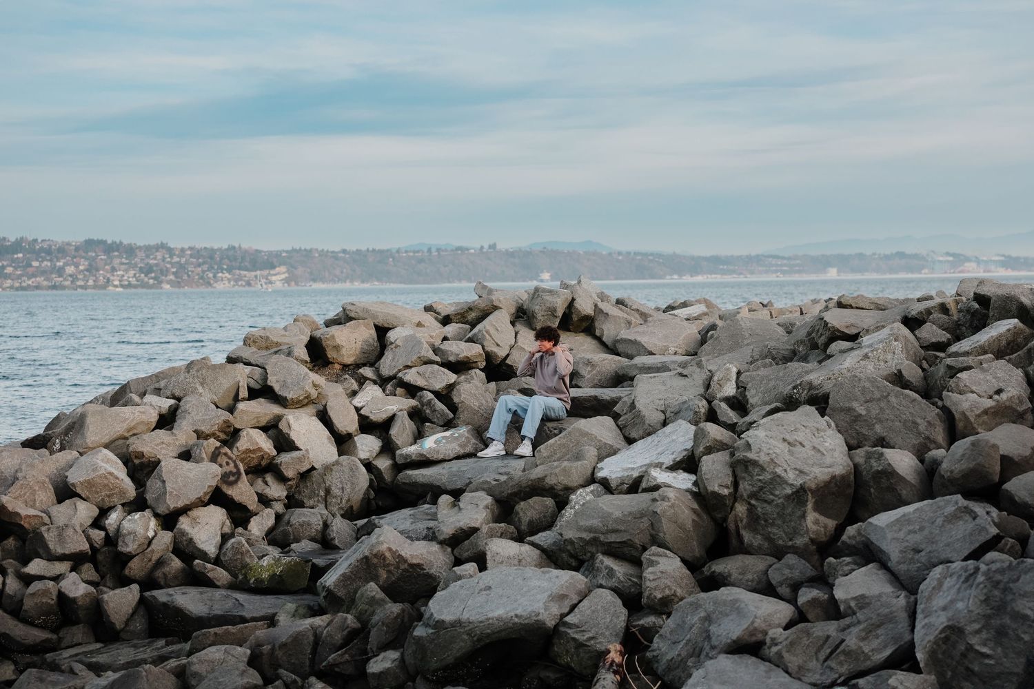 Panoramic view of a rocky seawall with dark boulders stretching along a cloudy coastline.