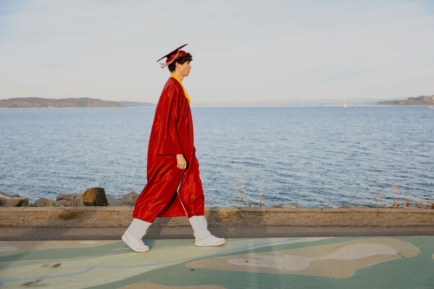 A person in a red coat walks along a serene coastal pathway with ocean views on a cloudy day.