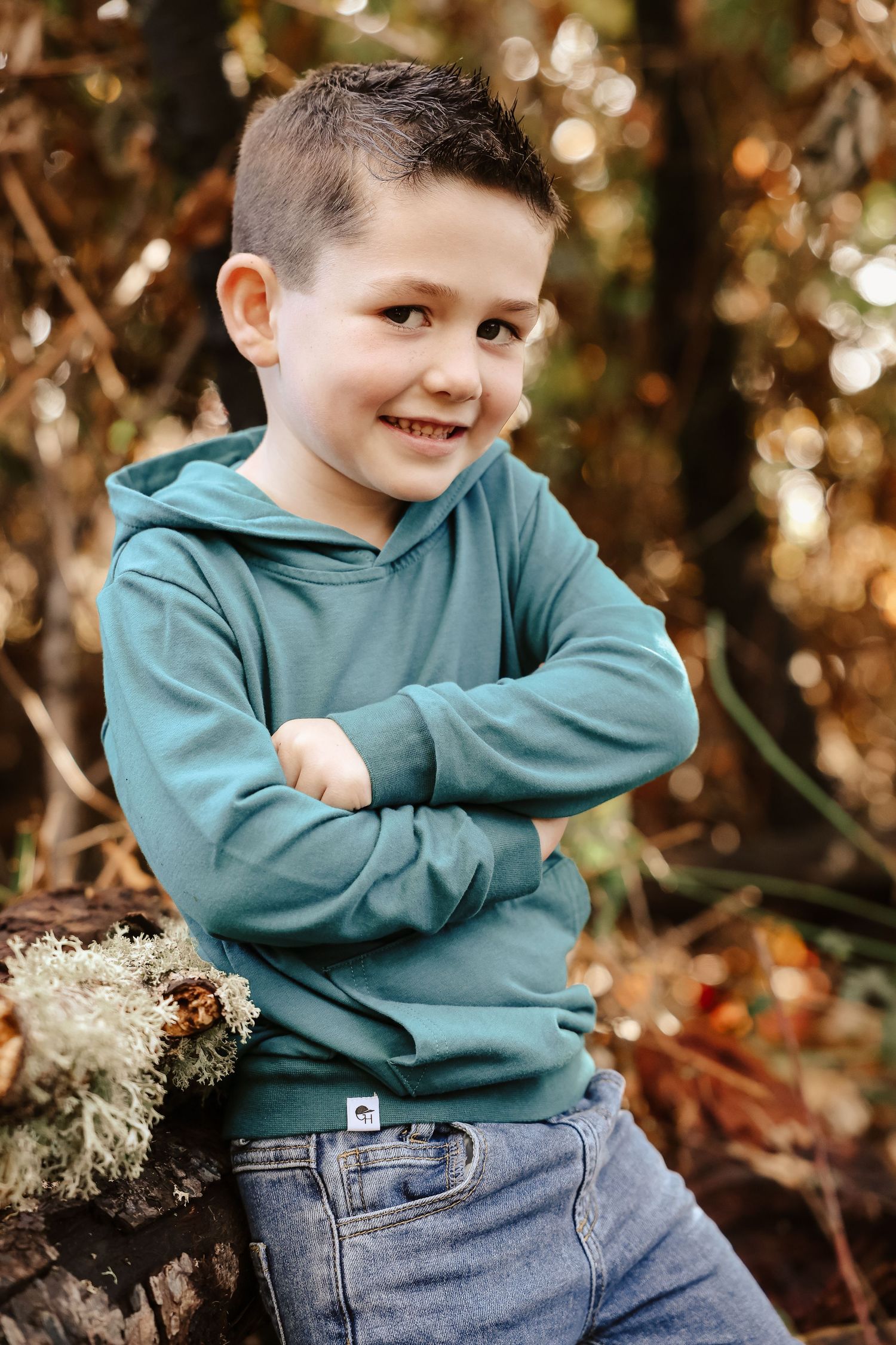 A child in a teal sweatshirt and jeans poses playfully against an autumn background with bokeh lighting effects.
