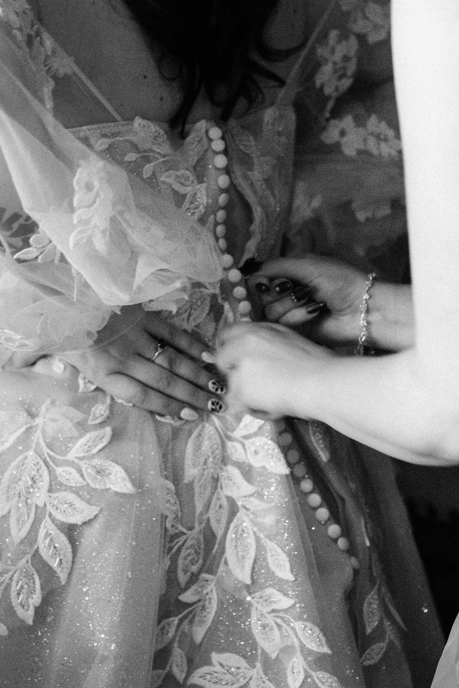 Close-up of hands fastening buttons on a delicate floral lace wedding dress.