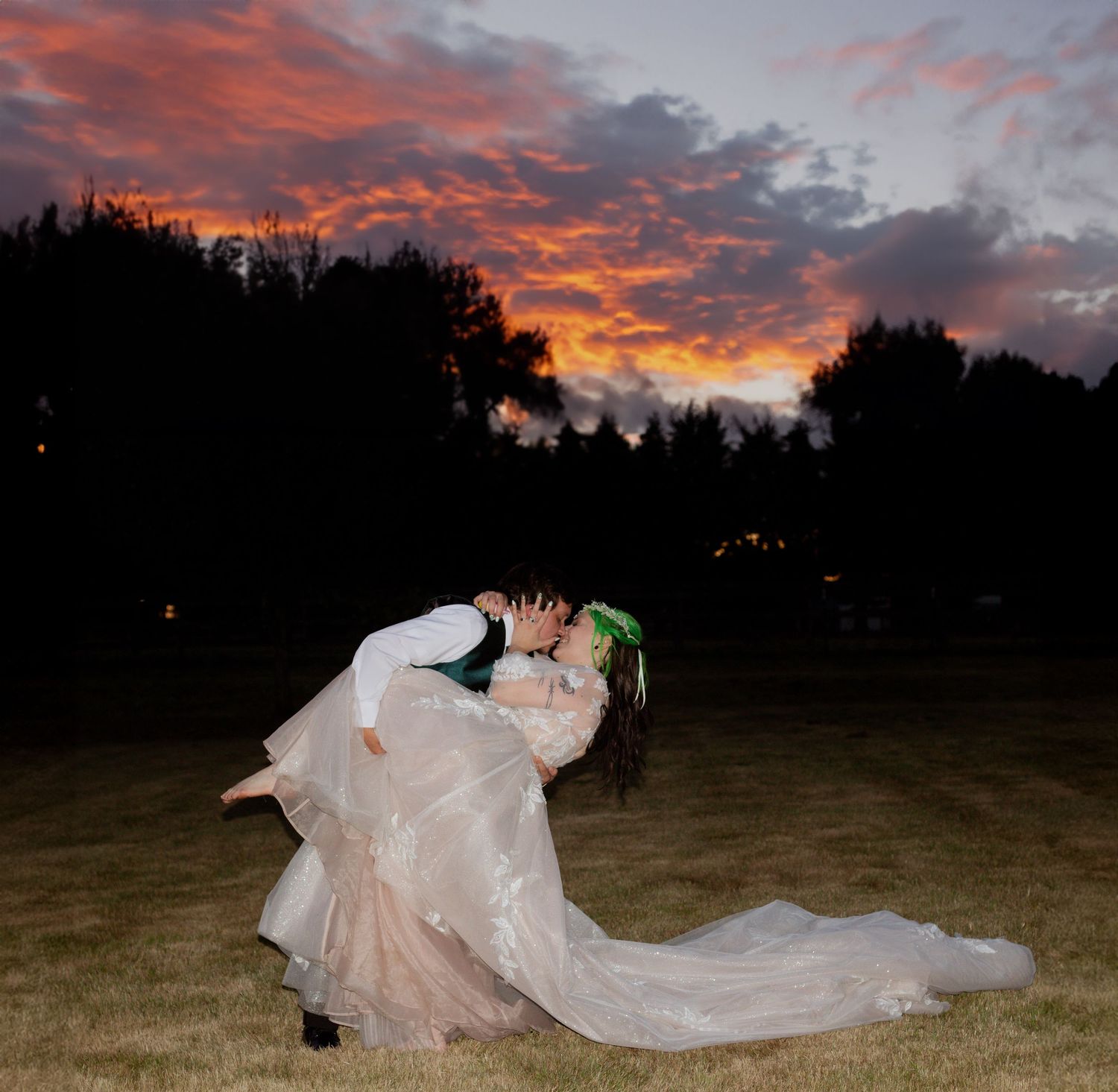 A romantic dance dip silhouetted against a dramatic sunset sky with vibrant orange clouds.